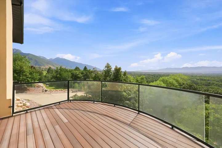 Curved deck with wood-finish flooring, glass railing, and mountain scenery