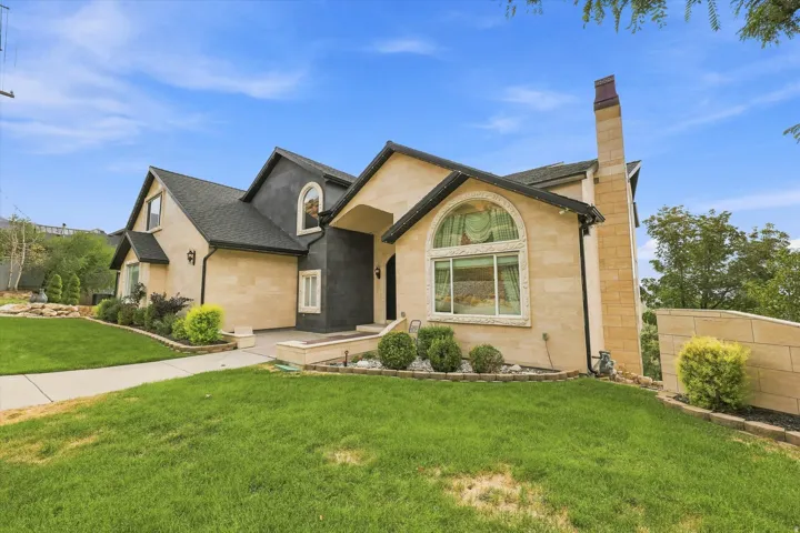 Stucco exterior with stone accents, arched window, prominent chimney, and a landscaped front yard with a concrete walkway