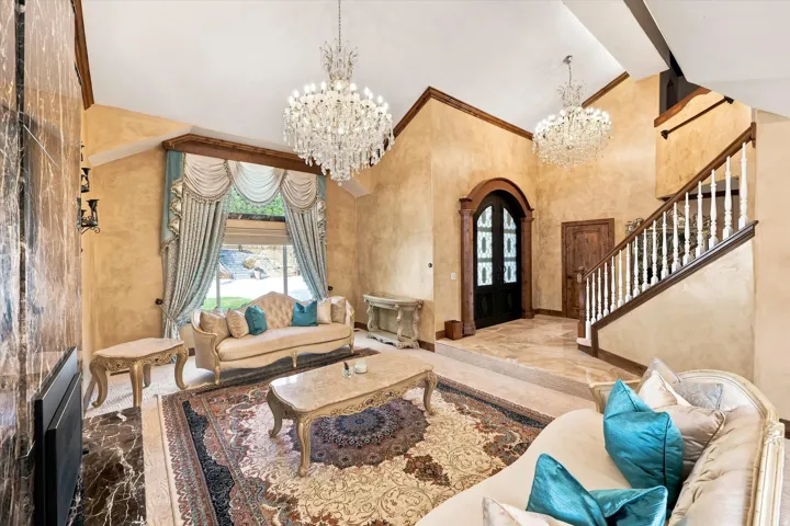 Vaulted ceilings, crystal chandeliers, staircase with dark wood handrail, arched doorway, and stone-finish flooring