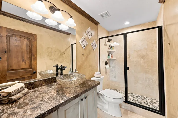 Walk-in shower with a glass enclosure, pebble-stone shower floor, and tiled walls