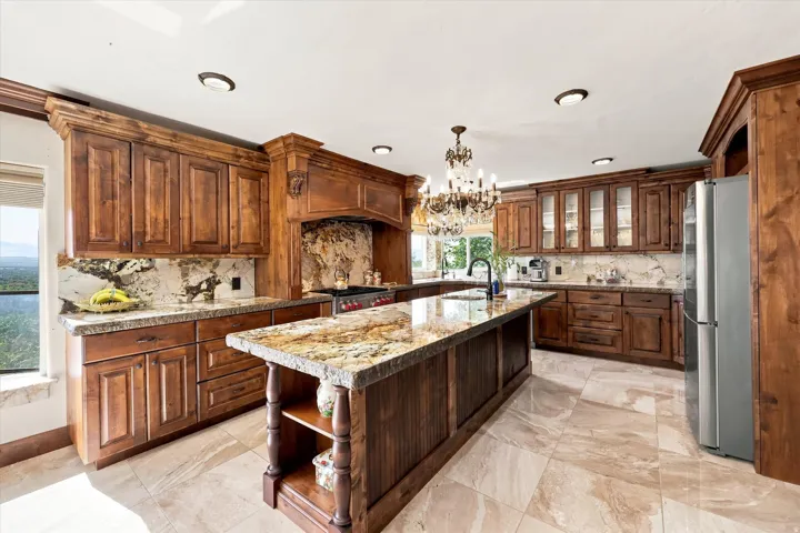 Gourmet kitchen featuring custom wood cabinetry, granite countertops, a large center island, built-in stainless steel appliances, and tile flooring