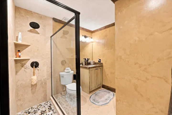 Frameless glass shower enclosure with a pebble-tiled shower floor and built-in wall shelves