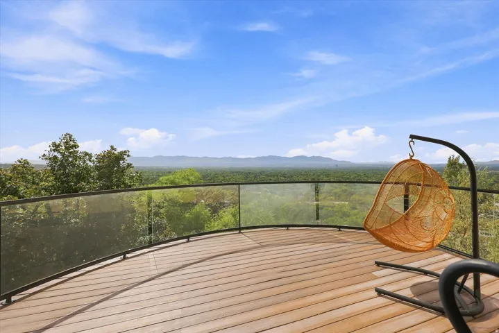 Curved outdoor balcony with wood-finish decking and clear glass railings, overlooking a distant mountainous landscape