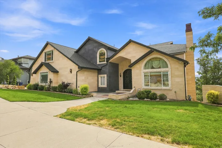 Stucco and stone exterior with arched windows, a covered entry, and a prominent chimney feature