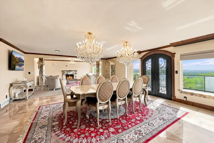 Travertine-style tile flooring, two crystal chandeliers, a built-in fireplace, and ornate double doors