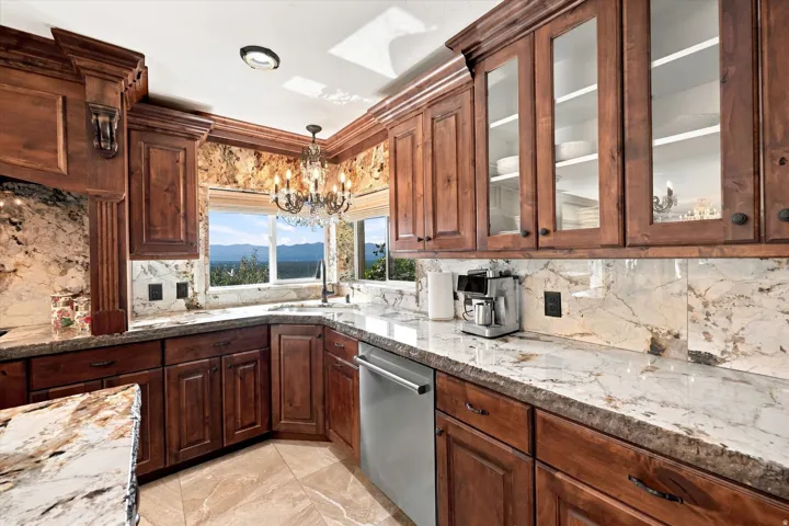 Wood cabinetry with glass-front upper cabinets, stone countertops, and a coordinating stone backsplash