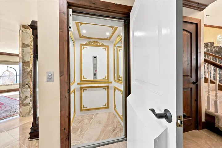 Custom elevator with ornate gold detailing, recessed lighting, and a stone-finish floor