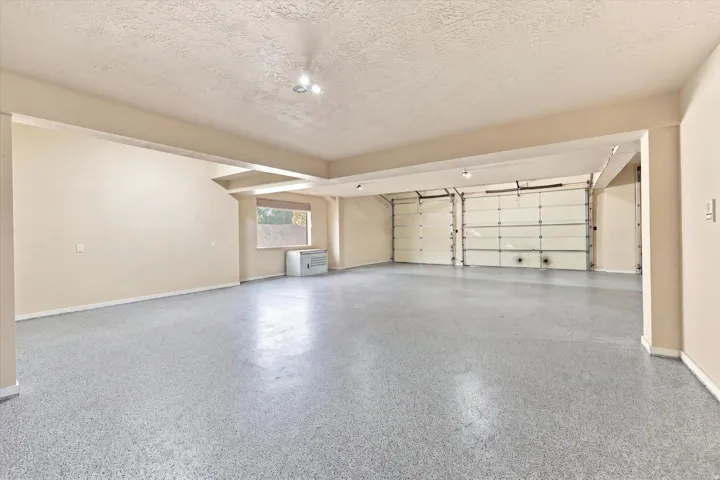 Spacious garage with multiple overhead doors, light gray speckled flooring, recessed lighting, and a single window