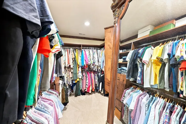 Custom built-in shelving, extensive hanging rod storage, recessed ceiling lighting, and wood-finish trim