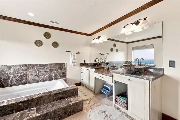 Spacious bathroom featuring a built-in jetted tub with tiled surround, dual vanity with vessel sinks, expansive wall mirror, and overhead vanity lighting