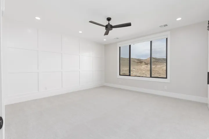 Recessed lighting, ceiling fan, expansive window with exterior scenery, wall paneling, and neutral carpeting