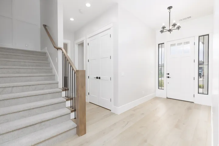 Entryway featuring a white paneled door with sidelights, wood-finish flooring, a contemporary chandelier, and a carpeted staircase with a wood and metal railing