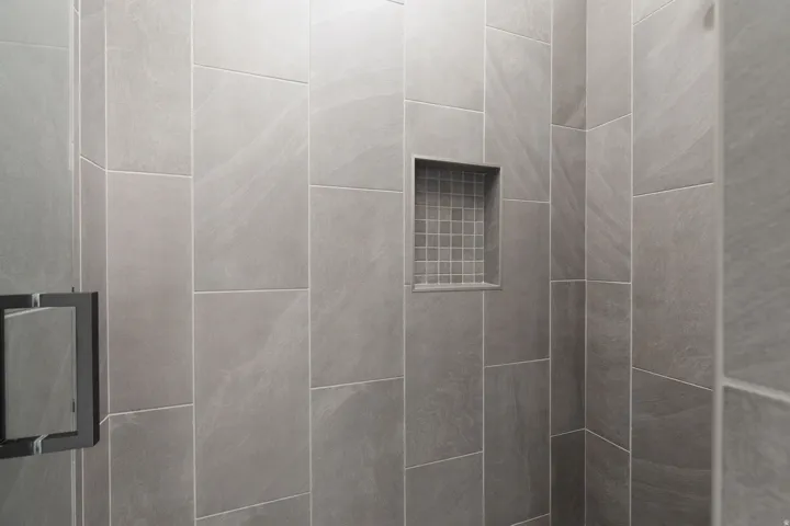 Shower enclosure with floor-to-ceiling tile, built-in niche with mosaic tile, and a dark-framed glass door