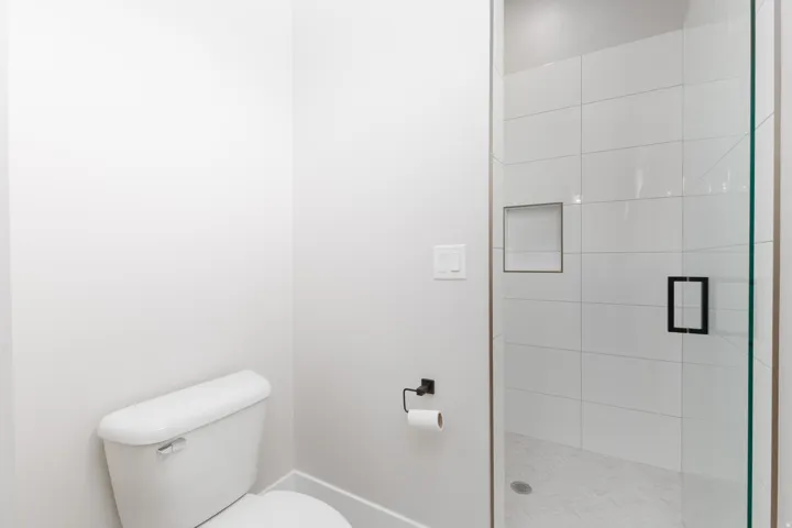 Glass-enclosed shower with white tiled walls, a built-in shower niche, and a matte black handle
