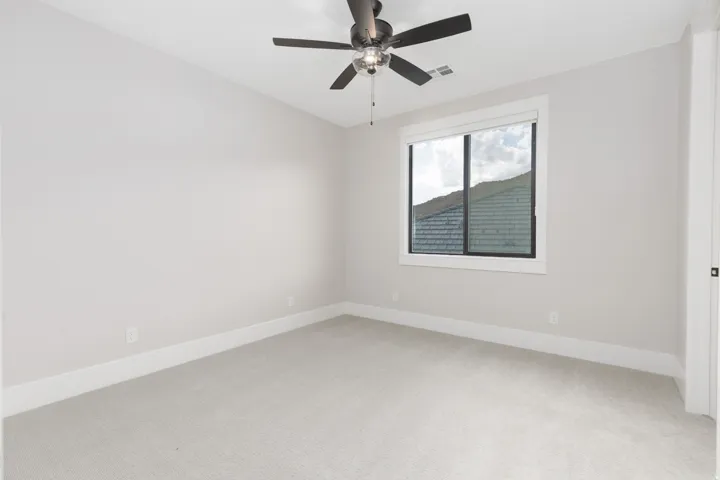 Neutral wall paint, carpet flooring, a window with white trim, and a ceiling fan with light fixture
