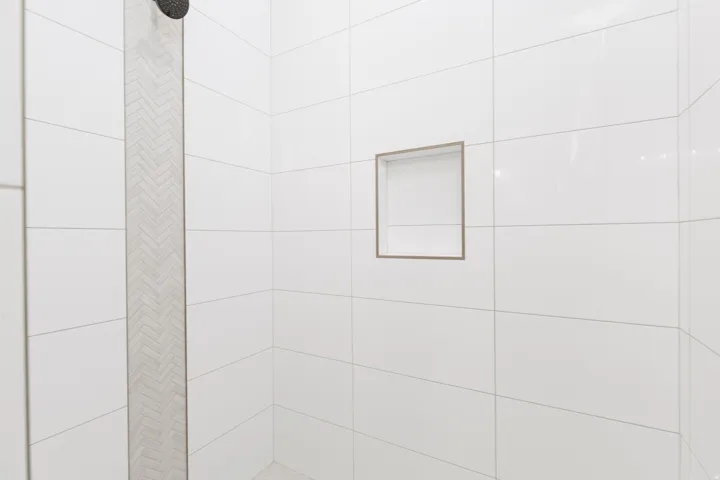 Shower enclosure with white subway tile, a recessed niche, herringbone accent tile, and a matte black showerhead