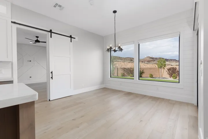 Light wood-finish flooring, a contemporary chandelier, large windows, a sliding barn door, and shiplap accent wall