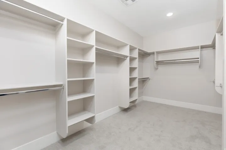 Built-in closet organization system featuring shelving, multiple hanging rods, and recessed lighting