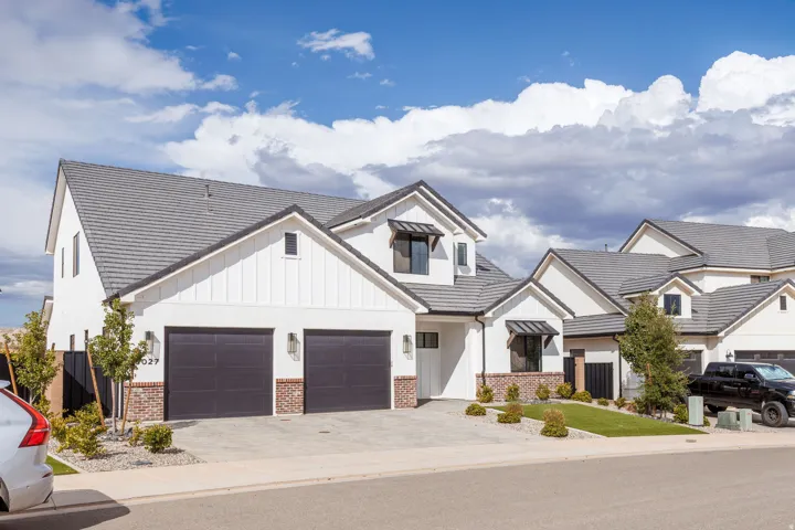 Modern farmhouse exterior with white siding, dark gray garage doors, brick accents, dark gray roof tiles, and a concrete driveway