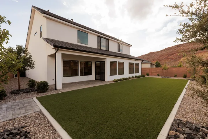 Two-story exterior with white stucco, covered patio with paver flooring, expansive artificial turf lawn, and a natural wood privacy fence