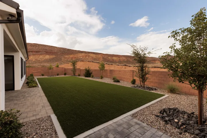 Expansive backyard featuring artificial turf, paver patio, gravel landscaping, a block privacy fence, and mature trees