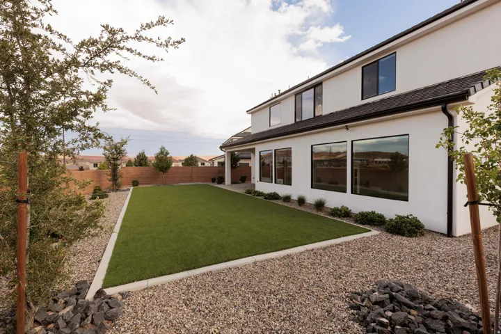 Expansive backyard featuring a rectangular artificial turf lawn, decorative gravel, and mature trees