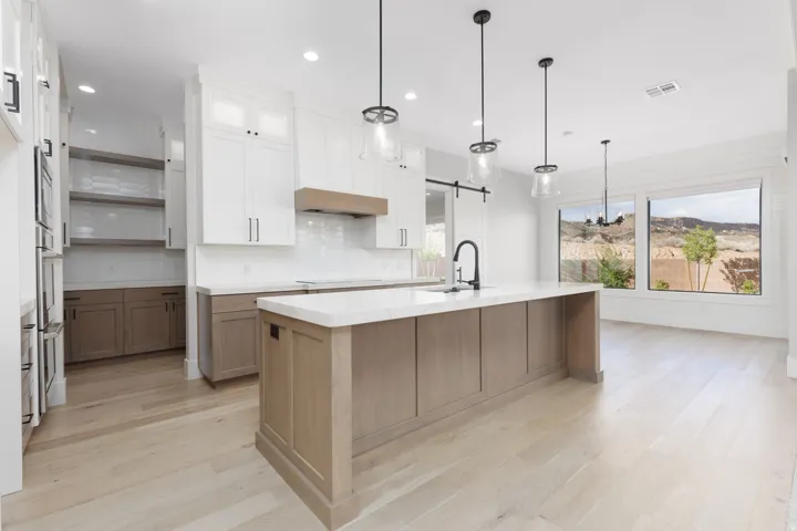 Kitchen featuring a large island with sink, light wood-finish flooring, white upper cabinetry, and a full suite of stainless steel appliances