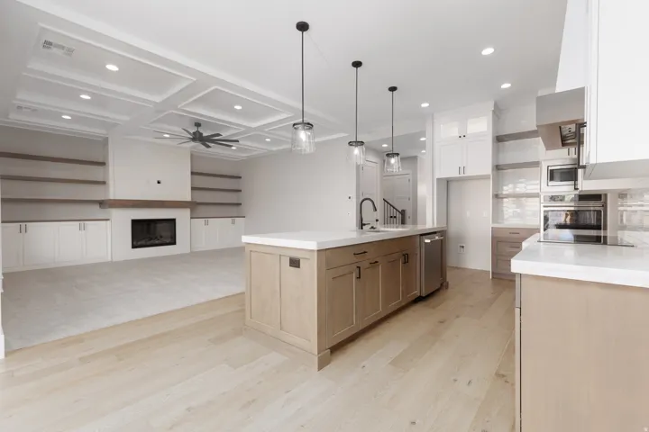 Open-concept kitchen and living area featuring wood-finish flooring, a coffered ceiling, built-in shelving, a fireplace, and stainless steel appliances