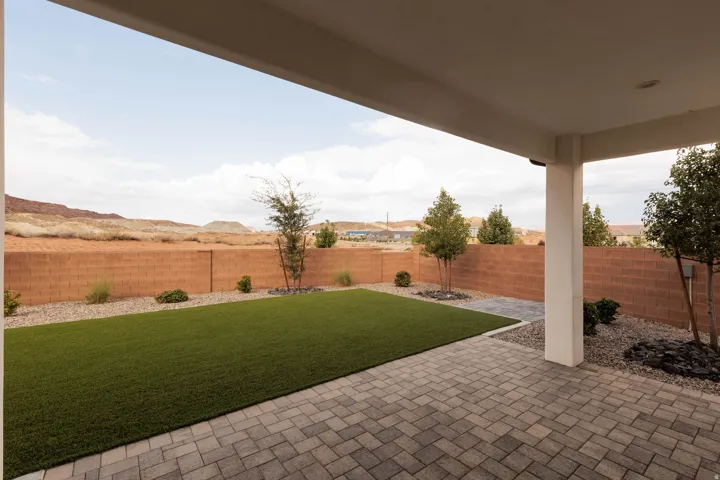 Covered patio with paver flooring, artificial turf lawn, and a block perimeter wall
