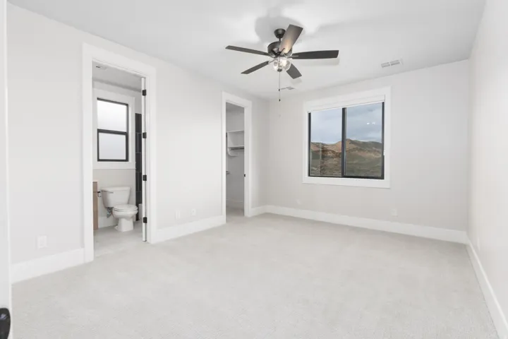Carpeted room featuring a ceiling fan, a window with exterior scenery, and access to a bathroom with a window, and a separate closet with shelving