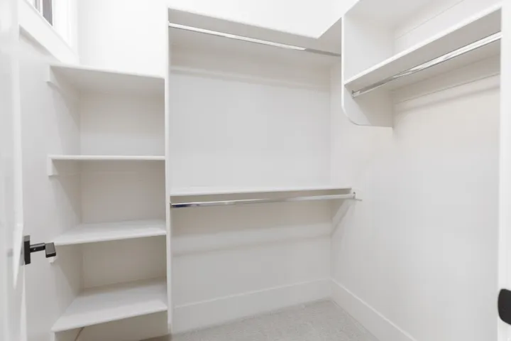 Walk-in closet with integrated shelving units, multiple clothing rods, and light-toned carpeting