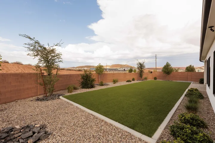 Expansive backyard featuring artificial turf, gravel landscaping, a block privacy fence, and mature plantings