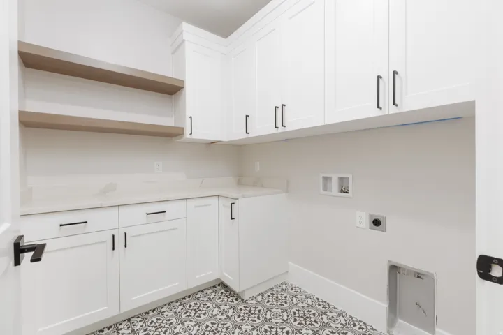 White cabinetry with matte black hardware, light-toned countertops, wood-finish floating shelves, and patterned floor tile