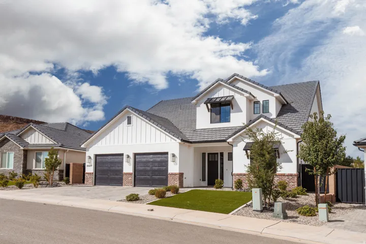 Modern farmhouse exterior with white siding, dark roof, brick accents, two-car garage, and a manicured artificial turf lawn