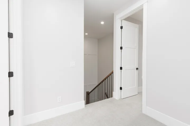 Plush carpeting, white paneled doors with matte black hardware, recessed lighting, and a staircase with dark wood handrails and black iron balusters