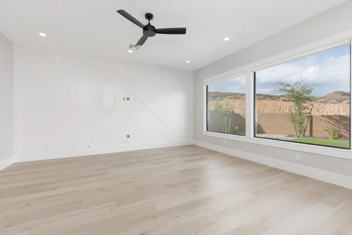 Expansive room featuring light wood-finish flooring, a decorative accent wall, a modern ceiling fan, recessed lighting, and large picture windows