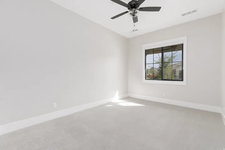 Carpeted room featuring a ceiling fan, a large window with black framing, and neutral wall tones