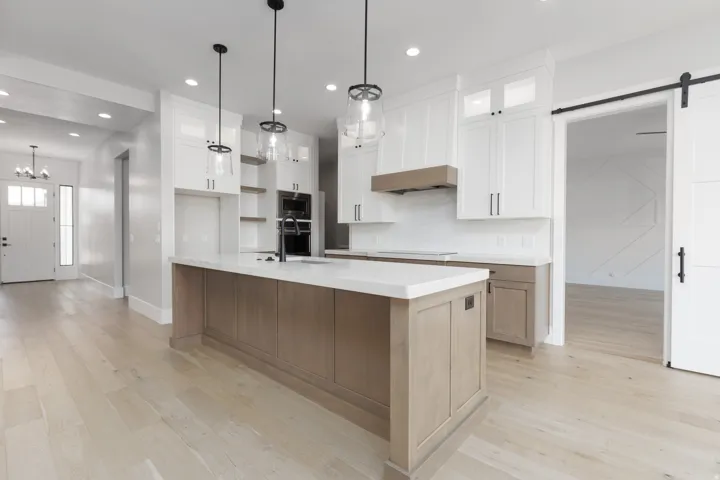 Expansive kitchen with a large central island, white shaker cabinetry, integrated double ovens, and a wood-finish range hood