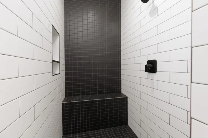 Walk-in shower featuring white subway tile walls, a built-in bench with black mosaic tile, a recessed shower niche, and matte black fixtures