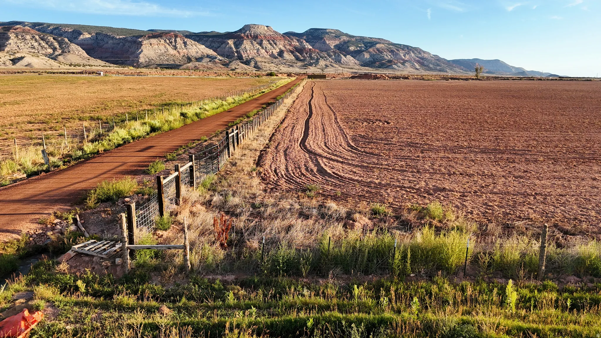 Expansive land parcel featuring a visible dirt road, fenced perimeter, and distant mountain range