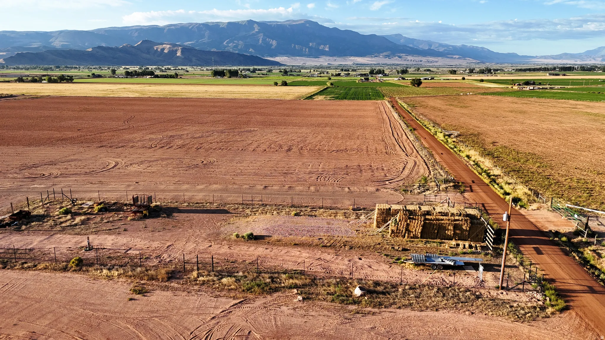 Expansive land featuring a dirt road, partial fencing, and distant mountains