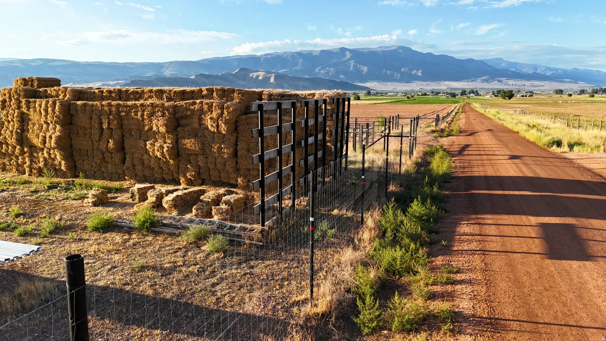 Expansive dry land with a dirt road, partial fencing, and distant mountains