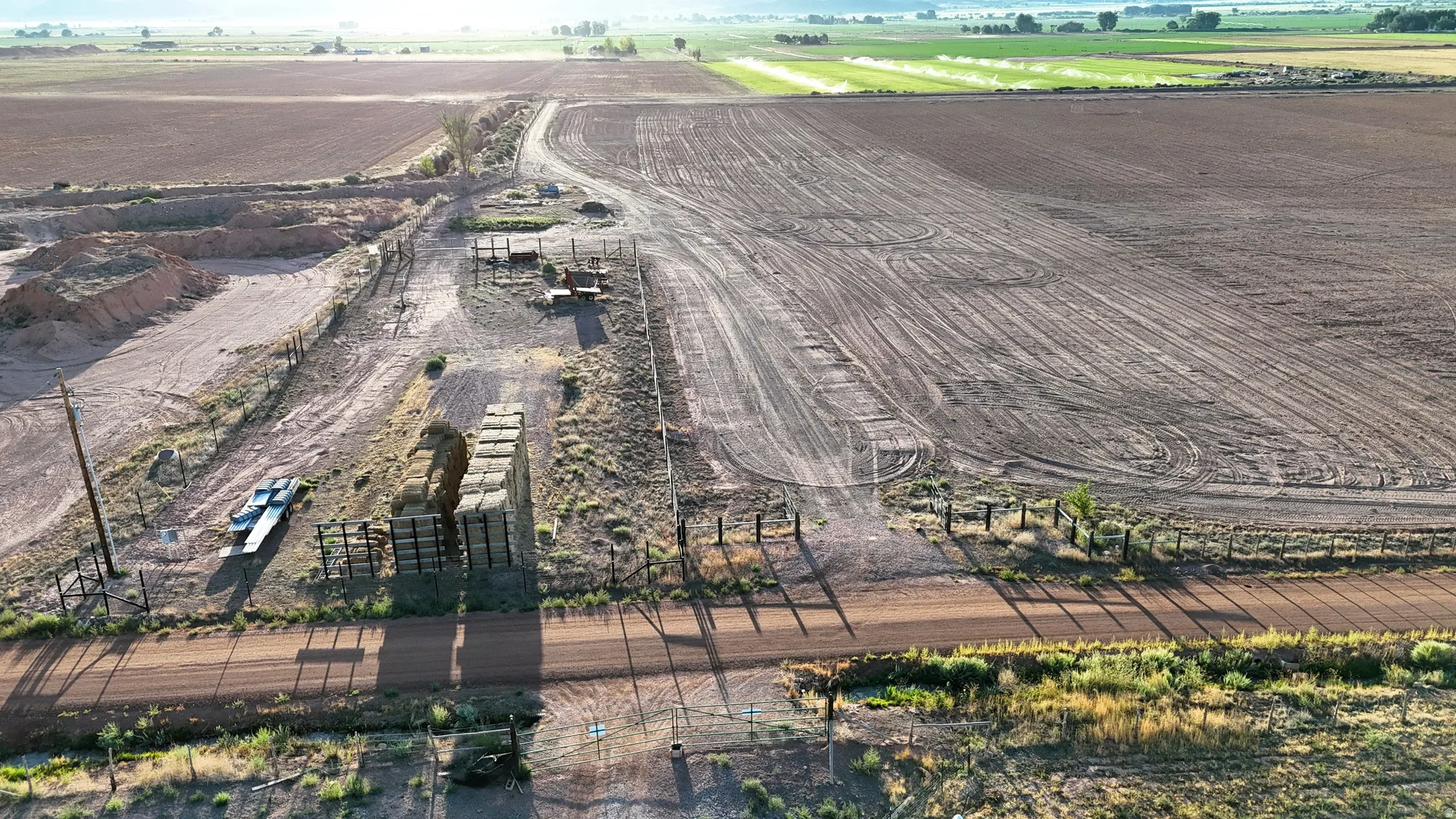 Expansive tilled agricultural land, fenced perimeter, dirt road access, and scattered hay bales
