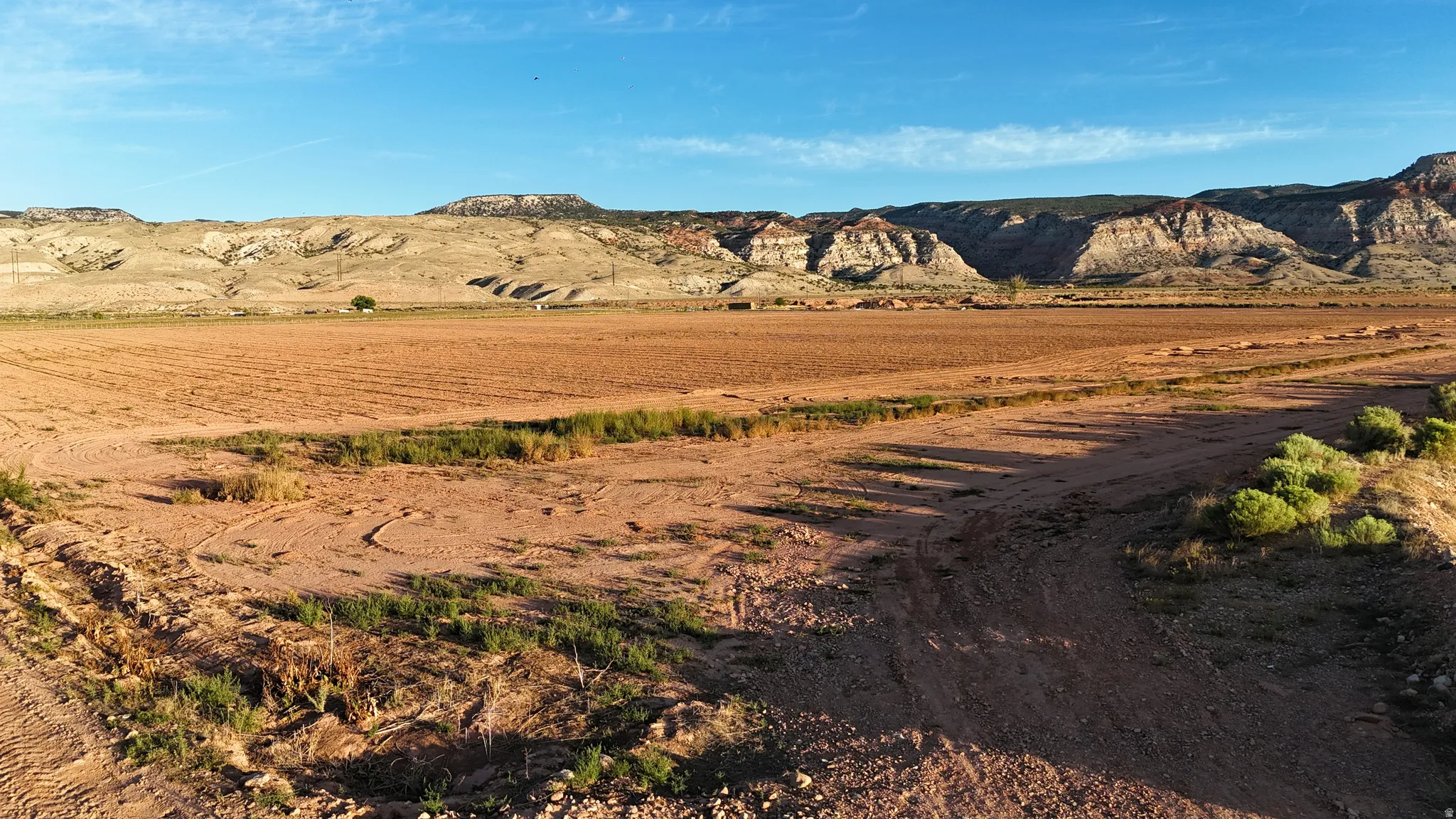 Expansive undeveloped land featuring a cleared field, natural terrain, and distant mountain backdrops under a clear sky