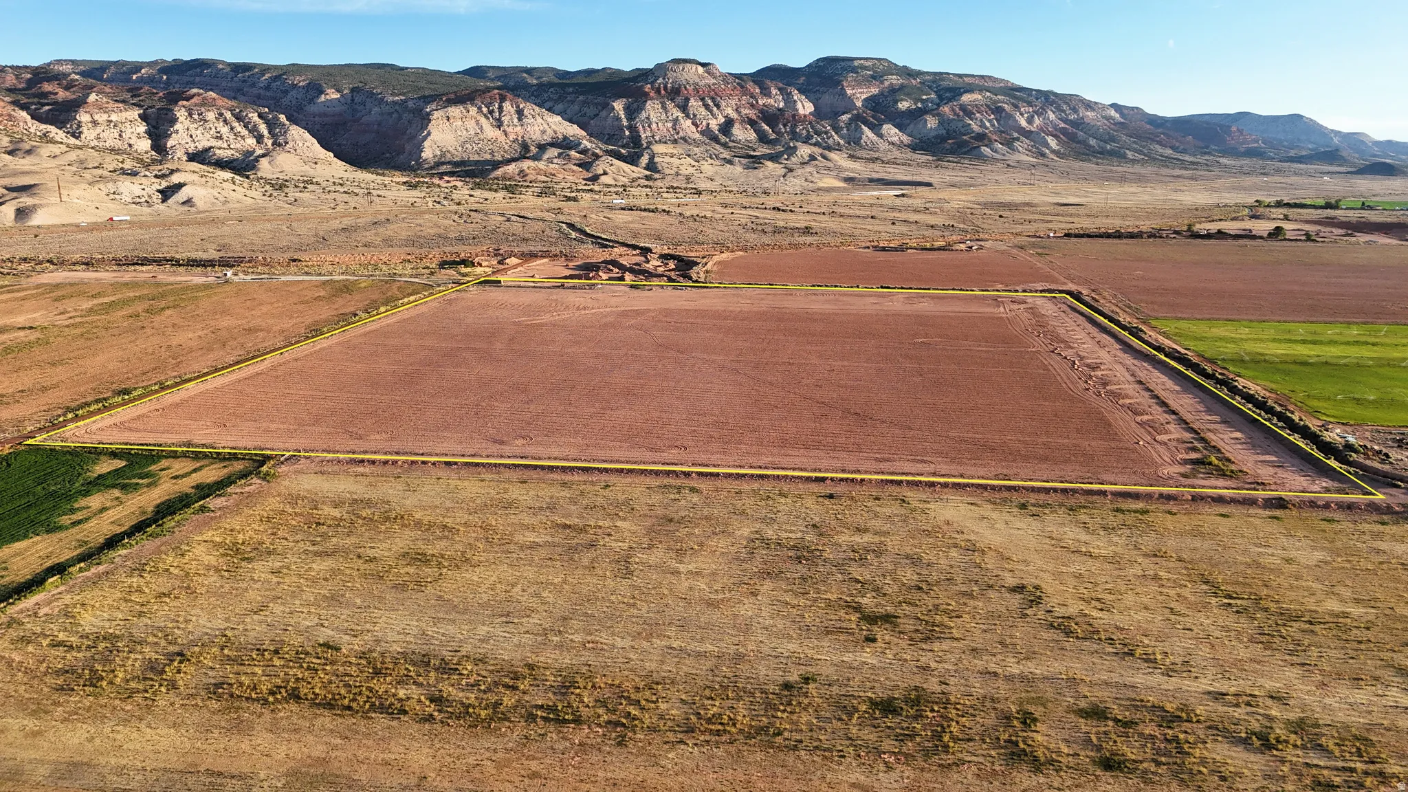 Expansive agricultural land featuring a tilled field, an irrigated field, and surrounding natural terrain