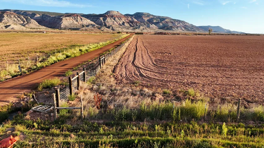 Expansive land parcel featuring a visible dirt road, fenced perimeter, and distant mountain range