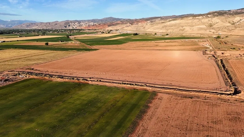 Expansive land parcel featuring prepared earth, surrounding cultivated fields, and distant mountain backdrops