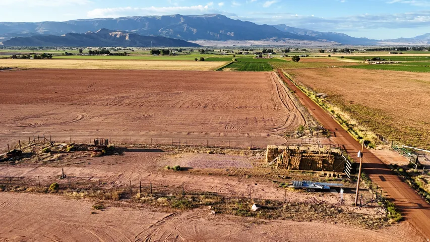 Expansive land featuring a dirt road, partial fencing, and distant mountains
