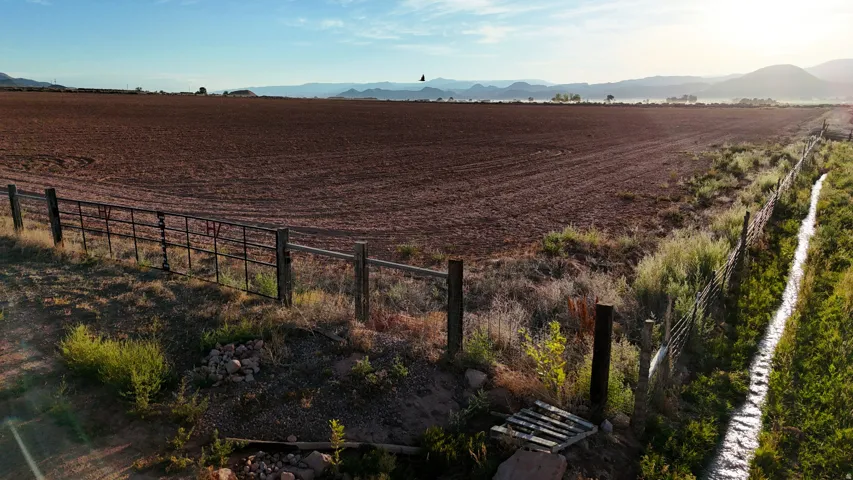 Expansive open land with tilled soil, perimeter fencing, and a visible irrigation ditch