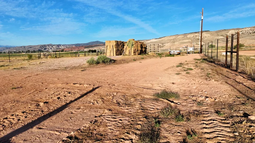 Expansive land featuring a dirt road, partial fencing, and distant mountains